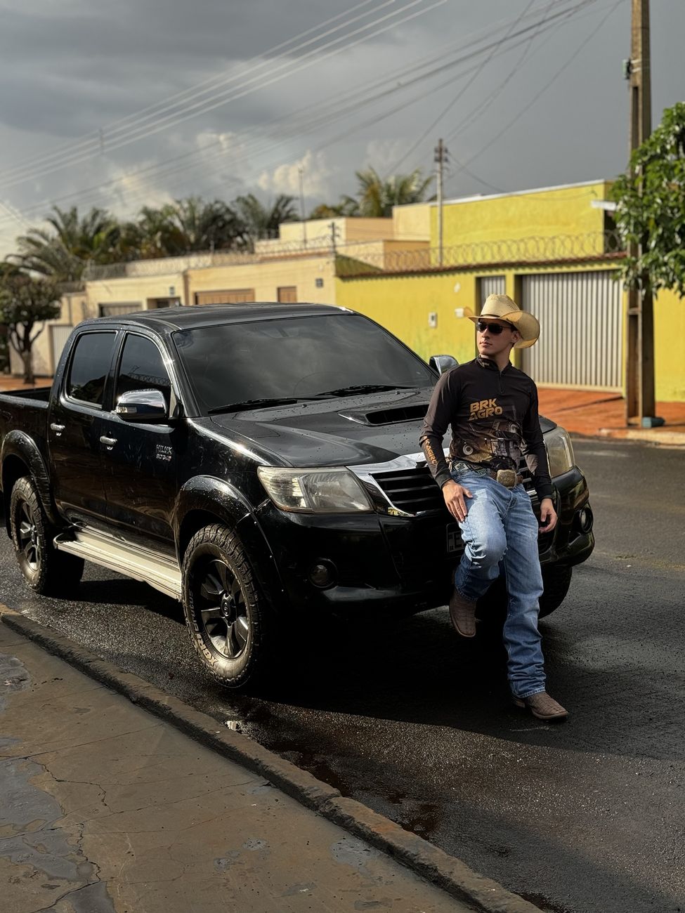 Wallas de chapéu encostado numa Hilux preta molhada de chuva